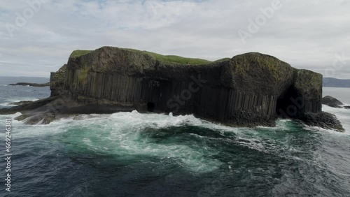 Aerial view flying over a Fingal's Cave on Staffa Island, west of Isle of Mull in Scotland. Calm waves touching the rocks. 4k video.