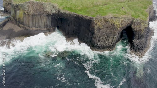 Aerial view flying over a Fingal's Cave on Staffa Island, west of Isle of Mull in Scotland. Calm waves touching the rocks.