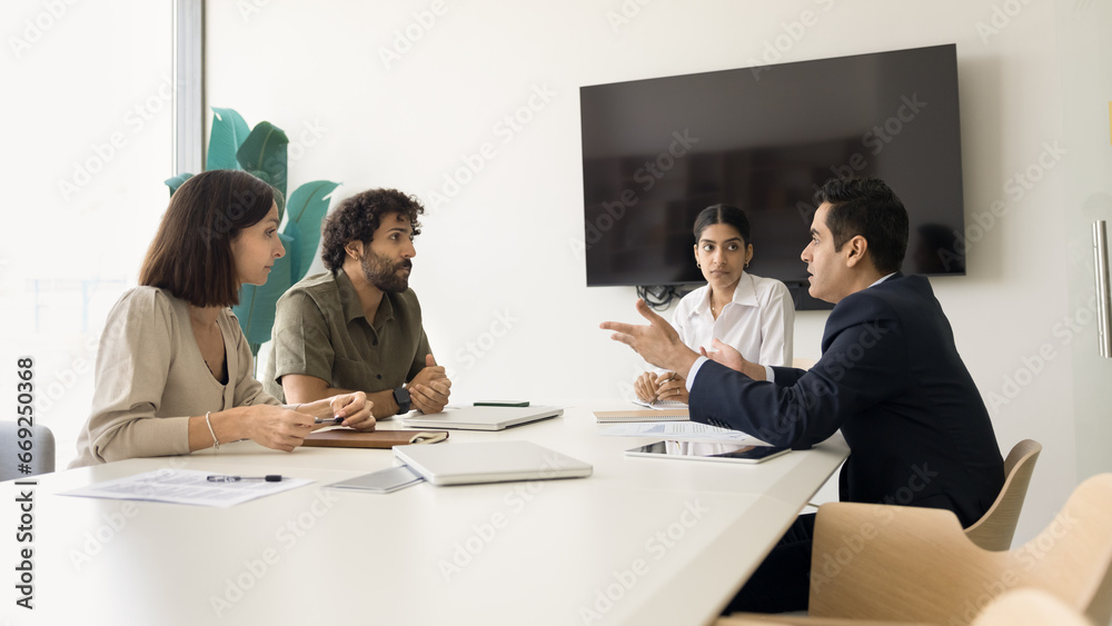 Serious diverse business colleagues discussing work on project, management strategy, meeting at table in boardroom. Young Indian leader woman holding negotiation of partners