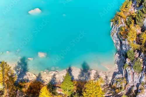 Vertical view of Azure water of Lake Sorapiss and coastal beach. Dolomites in autumn. Sunny day, contrast of colors, azure with orange. 