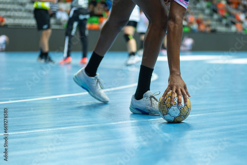 Handball woman player raises ball from parquet during the match.