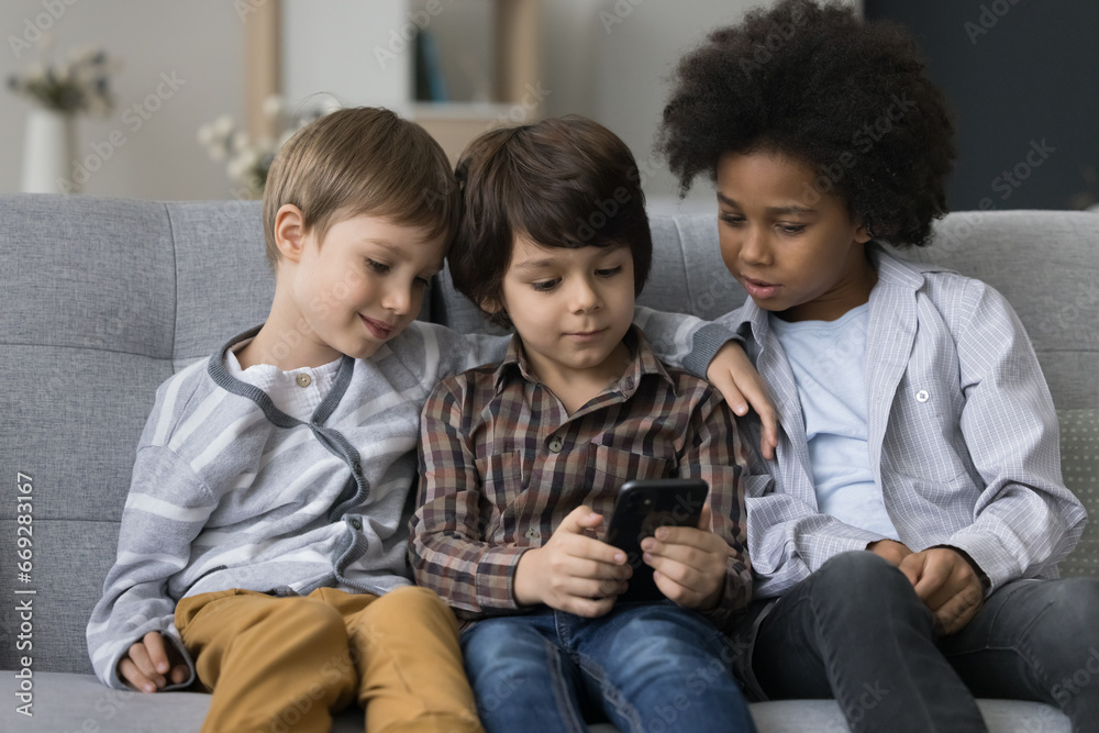 Three kids using smartphone together sitting on sofa, spend free time at home have fun with device, play cool new on-line games, friendly brothers watch funny videos in social network, browse internet Three kids using smartphone together sitting on sofa, spend free time at home have fun with device, play cool new on-line games, friendly brothers watch funny videos in social network, browse internet