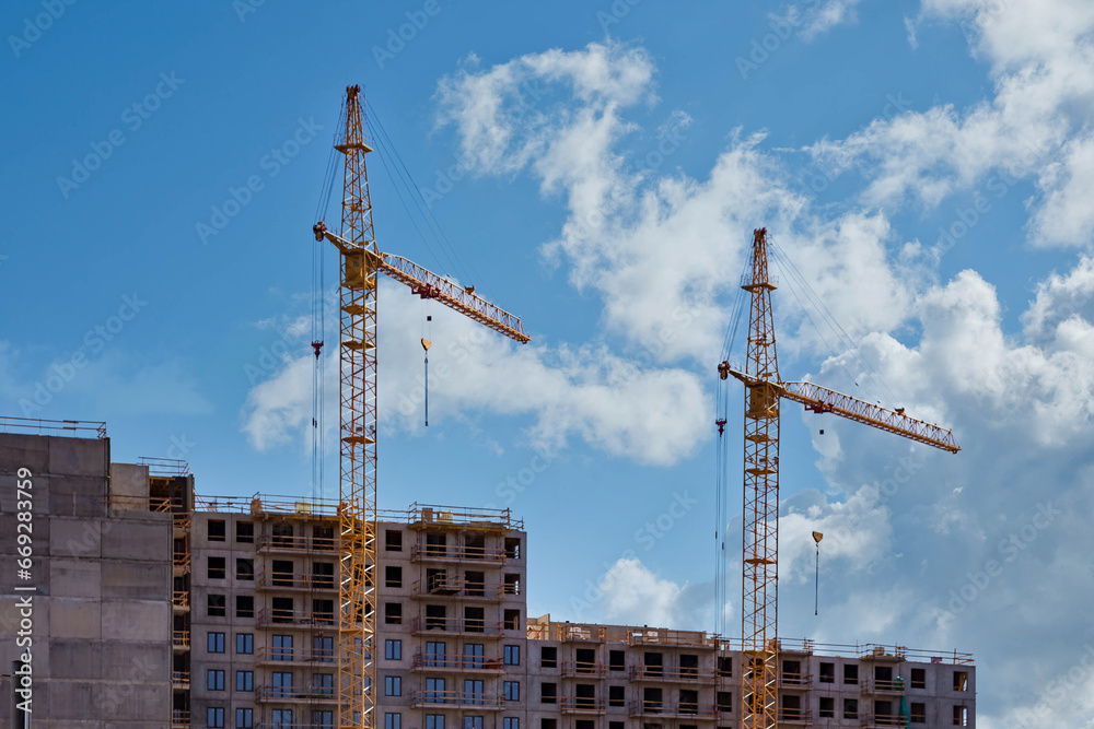 Panorama of construction crane work on creation site against blue sky background. View of industrial cranes. Concept of construction of apartment buildings and renovation of housing. Copy space