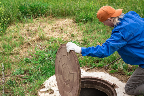 A plumber opens a manhole cover on a concrete well. Inspection and maintenance of water and sewer wells