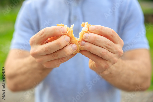 A man's hand breaks a croissant, snack and fast food concept. Selective focus on hands with blurred background