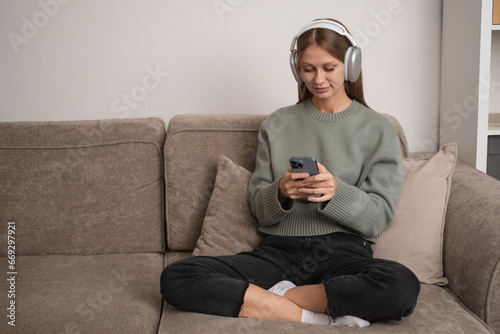 a happy girl sitting on the couch listening to music on wireless headphones. Young woman relaxing at home with music