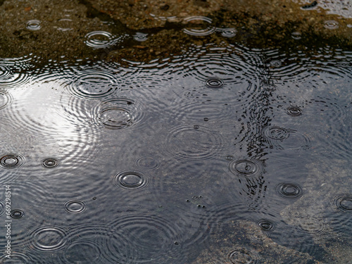 Raindrops falling into small puddle on the sidewalk on rainy day