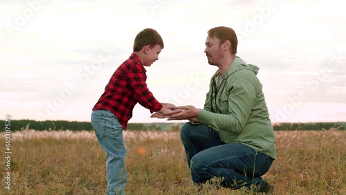 Positive boy gives high-five to father playing in middle of field in agricultural area