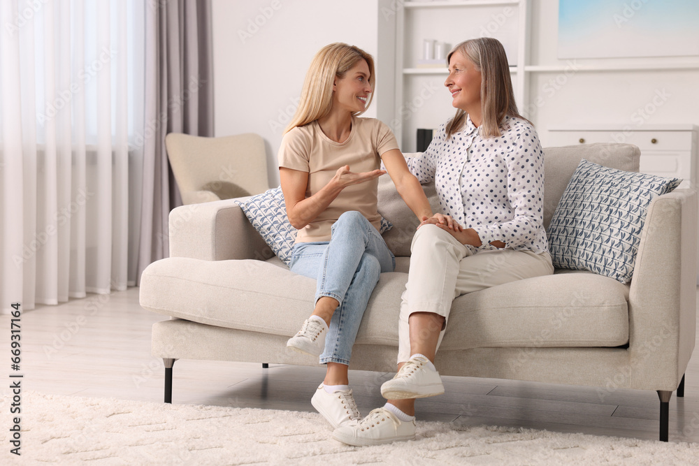 Happy mature mother and her daughter talking on sofa at home
