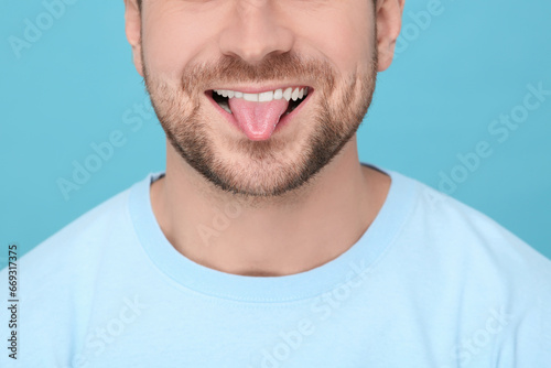 Man showing his tongue on light blue background, closeup