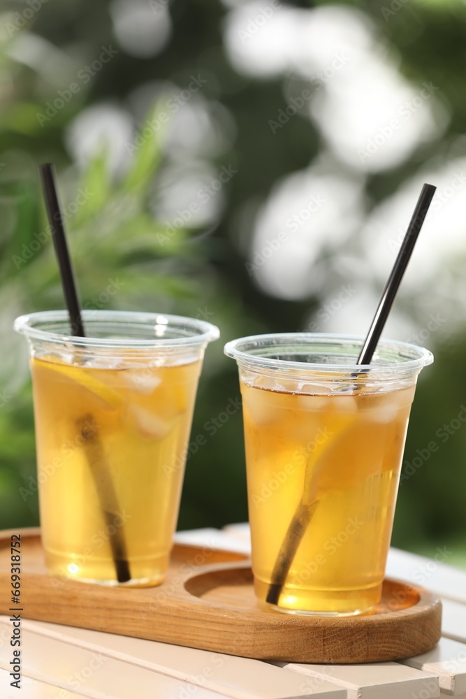 Plastic cups of tasty iced tea with lemon on white wooden table against blurred background Plastic cups of tasty iced tea with lemon on white wooden table against blurred background