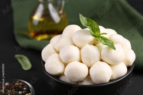 Tasty mozzarella balls and basil leaves in bowl, closeup. Space for text