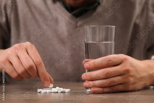 Man with glass of water and antidepressant pills at wooden table, closeup