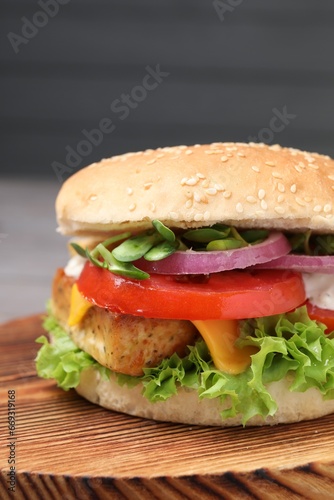 Delicious burger with tofu and fresh vegetables on wooden board, closeup
