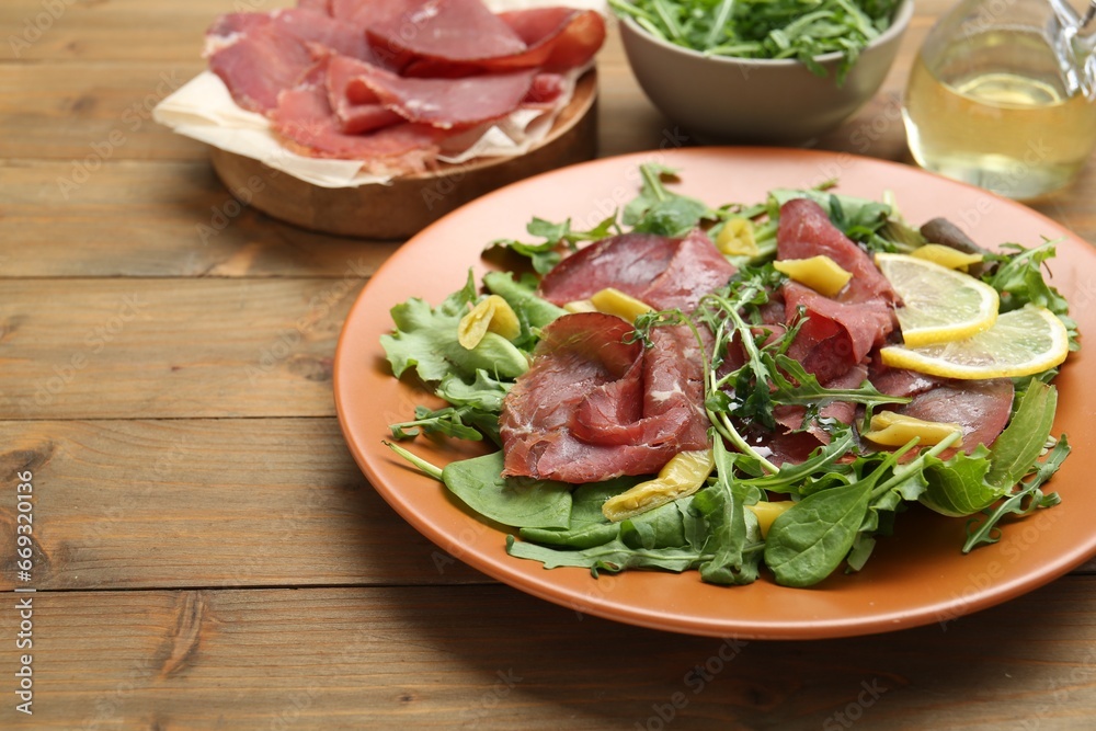 Delicious bresaola salad on wooden table, closeup. Space for text