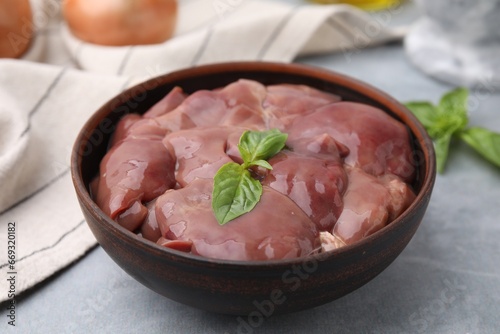 Bowl with raw chicken liver and basil on light grey table
