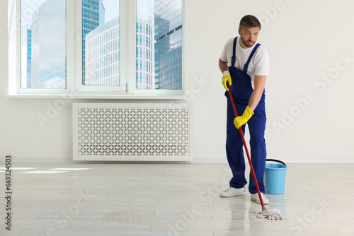 Man in uniform cleaning floor with mop indoors. Space for text