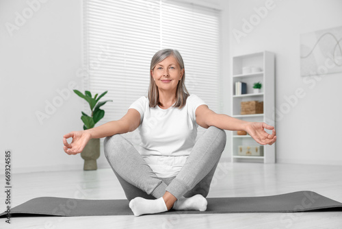 Fototapeta Naklejka Na Ścianę i Meble -  Happy senior woman practicing yoga on mat at home