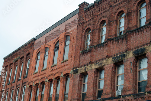 The exterior of multiple brown brick buildings with tall arched glass windows. The classic apartment buildings are adjoined with flat rooftops. The vintage structures have various shades of brick. 