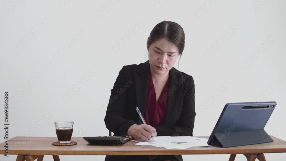 Business asian woman is calculating accounts and writing them down on a paperworks and has a tablet on the table., Successful professional woman working. Business asian woman is calculating accounts and writing them down on a paperworks and has a tablet on the table., Successful professional woman working.