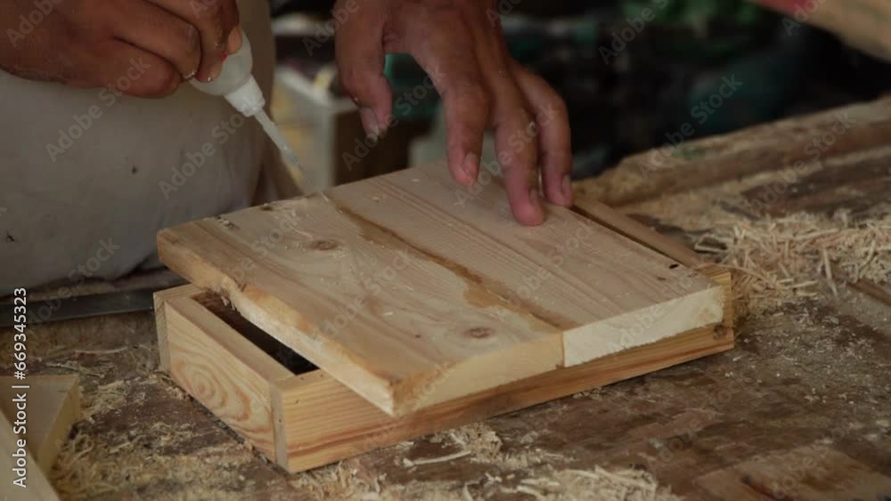 Close up of a carpenter working in a simple wood workshop. The workshop is full of piles of wood, circular saws, nailer guns, planing machines, drilling machines, wood glue and even wood paint Close up of a carpenter working in a simple wood workshop. The workshop is full of piles of wood, circular saws, nailer guns, planing machines, drilling machines, wood glue and even wood paint
