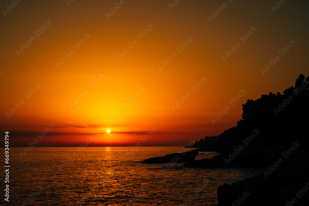 Sunset over the sea and dark hilly shore