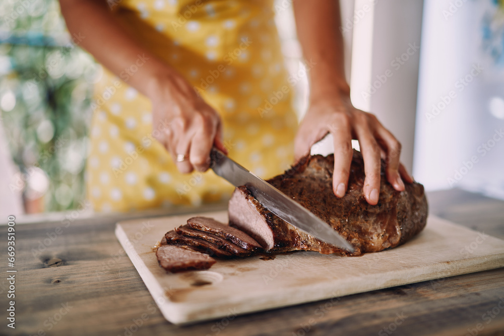 Housewife in an apron cuts juicy roast beef with a knife on a wooden cutting board