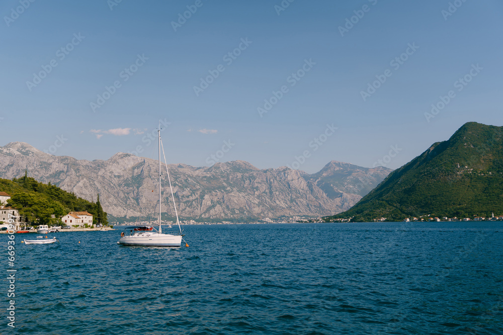 Sailing yacht is moored in the sea near the shore of an old town at the foot of the mountains