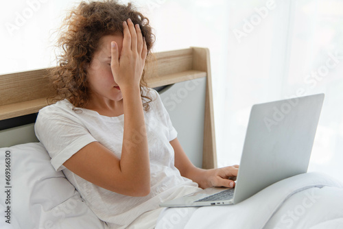 Young beautiful business woman has headache working with laptop while lying in bed in the morning after waking up.