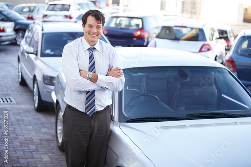 Portrait, luxury and a man arms crossed at a dealership for car sale in a commercial parking lot. Business, smile and automobile trade with a happy young salesman outdoor for transport service