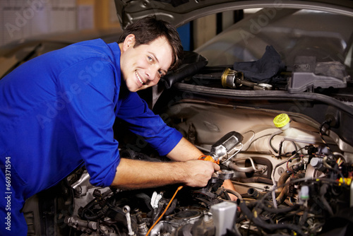 Portrait, smile and car with a mechanic man in a workshop as an engineer looking at the engine of a vehicle. Garage, service or repair with a happy technician working under the hood of an automobile