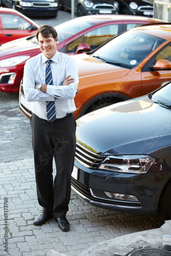 Portrait, smile and a man arms crossed in a parking lot for car sale at a commercial dealership. Business, luxury and automobile trade with a happy young salesman outdoor for transport rental © Duncan M/peopleimages.com