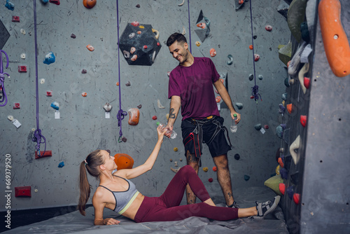A strong couple of climbers relax near artificial wall with colorful grips and ropes.