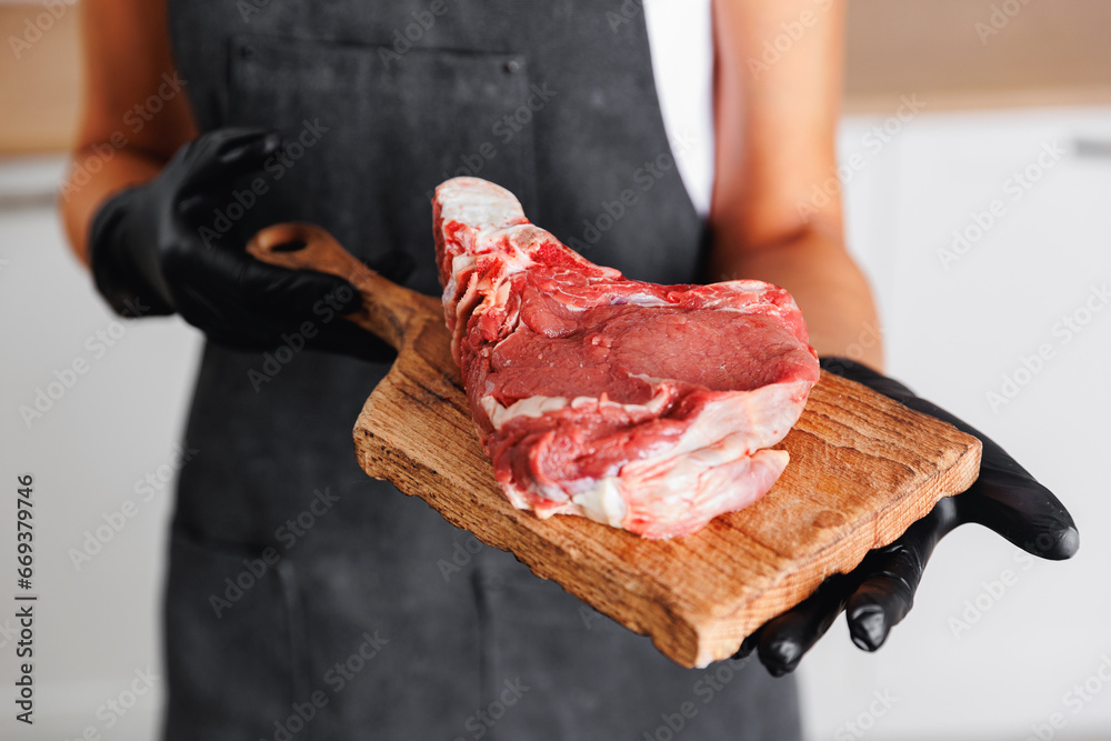 Butcher woman prepare fresh raw meat pork entrecote steak on wooden board, top view on dark background