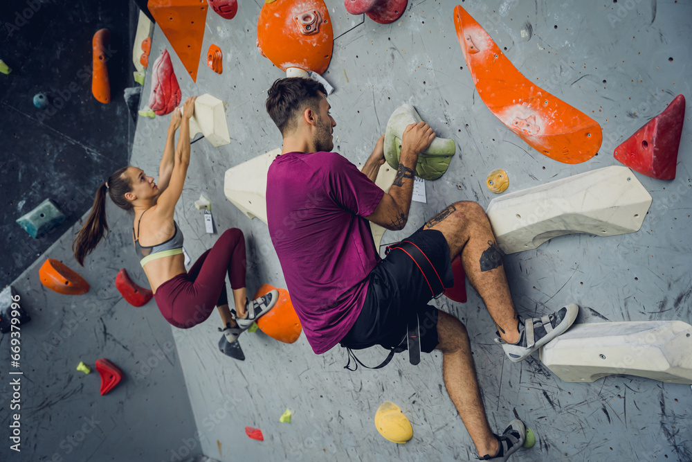 A strong couple of climbers climb an artificial wall with colorful grips and ropes. - obrazy, fototapety, plakaty 