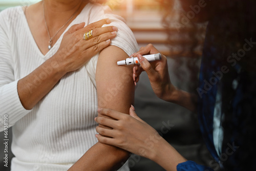 Cropped view of An African nurse or caregiver taking a blood sample of a senior woman's arm with a lancet pen. World Diabetic Day with Senior Diabetic Patient Concept