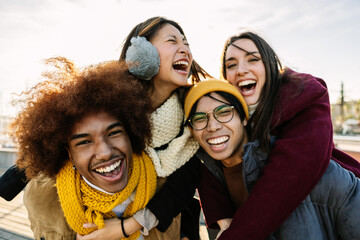 Young group of friends hanging out enjoying city break on winter vacation. Happy millennial diverse people laughing, social gathering in city street. Friendship and youth community concept.