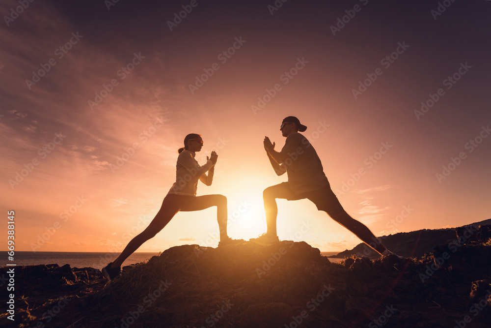 Young couple does yoga exercises on edge of mountain against sunrise