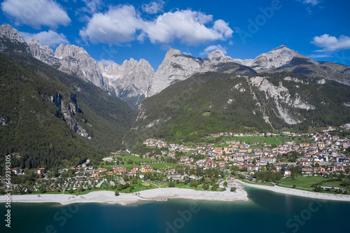 Aerial view of Lake Molveno, north of Italy in the background the city of Molveno, campanile basso, cima tosa Italian dolomites. Aerial view over the beautiful Molveno town and Molveno lake.