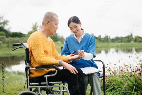 Asian young caregiver nurse support senior older male walking outdoors. Specialis doctor help and take care of elderly mature. Nursing home hospital garden