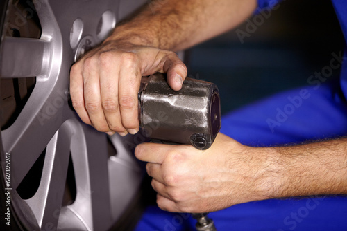 Hands, mechanic and change wheel in shop, electric drill and car service or auto repairs for maintenance. Technician, person and tire safety for automobile, rim and vehicle inspection in workshop