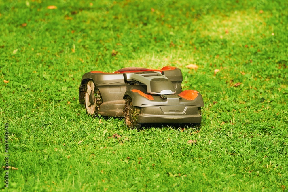 Fototapeta premium Robotic lawn mower on grass, side view. Close up isolated of automatic lawn mower. Smart lawn caring. Electronic grass trimmer.