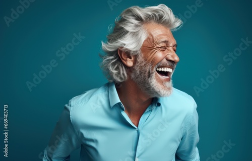 A joyful older man with wild silver hair laughing wholeheartedly against a vibrant blue background. Ideal for conveying happiness, aging gracefully, and positive emotions. photo