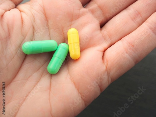 Hand holding three yellow and green medical capsule pills  photo