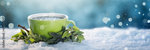 Green tea cup with mint leaves on snowy surface. Blurred winter background. Christmas and New Year. Suitable for holiday greetings, promotions, or banner with free space for text