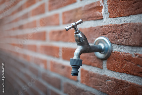 Close-up of metal outdoor tap on bricks wall.