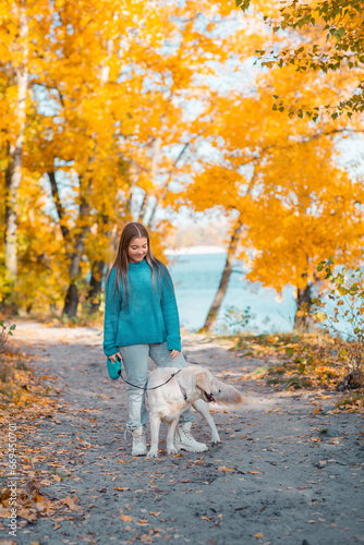 Wallpaper Mural A girl in an autumn park walks with a golden retriever dog. There are a lot of fallen autumn leaves around. A river flows in the background. Torontodigital.ca