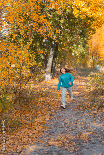 A teenage girl walks by herself in an autumn park near the river. She is joyful and happy.