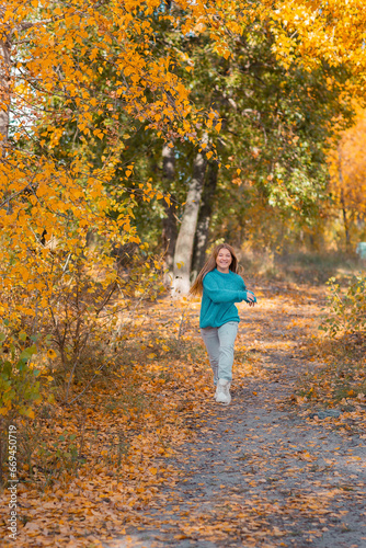 A teenage girl walks by herself in an autumn park near the river. She is joyful and happy.