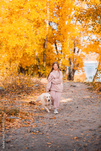 Wallpaper Mural A girl in an autumn park walks with a golden retriever dog. There are a lot of fallen autumn leaves around. A river flows in the background. Torontodigital.ca